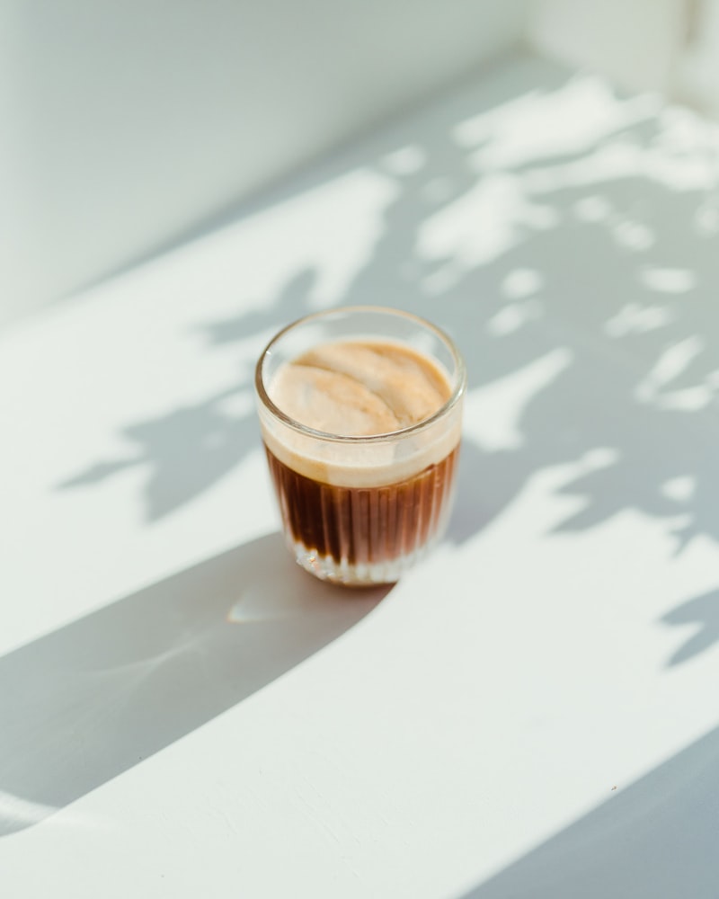 A cortado in a glass catching afternoon light and palm shadows